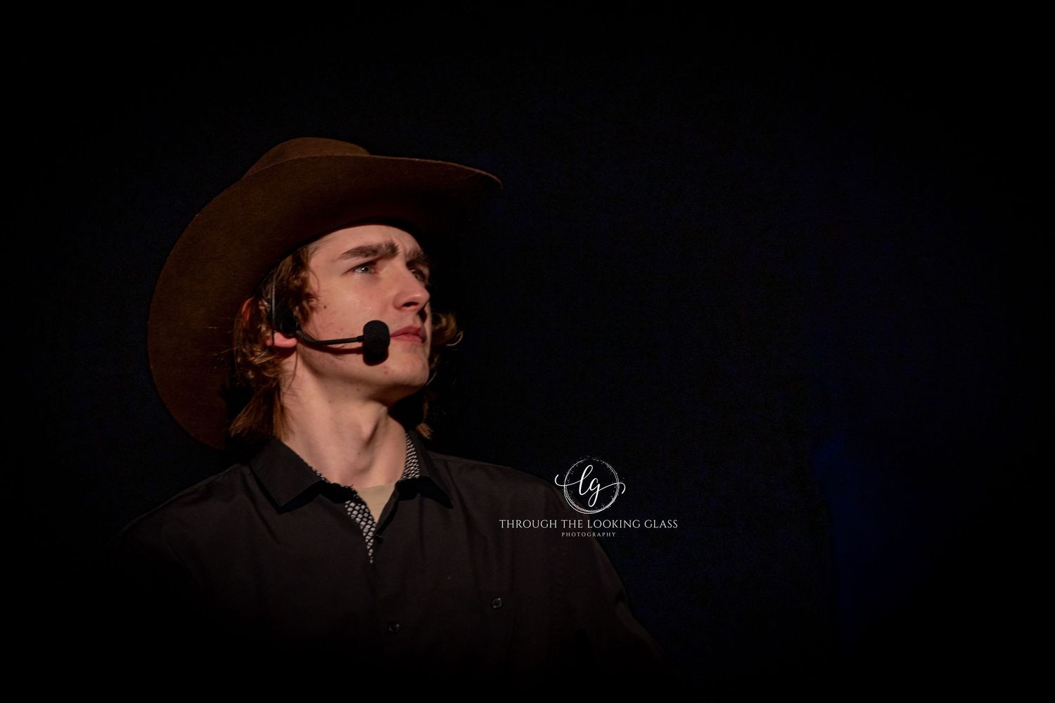 Western performer with headset microphone and brown cowboy hat in dramatic dark lighting.