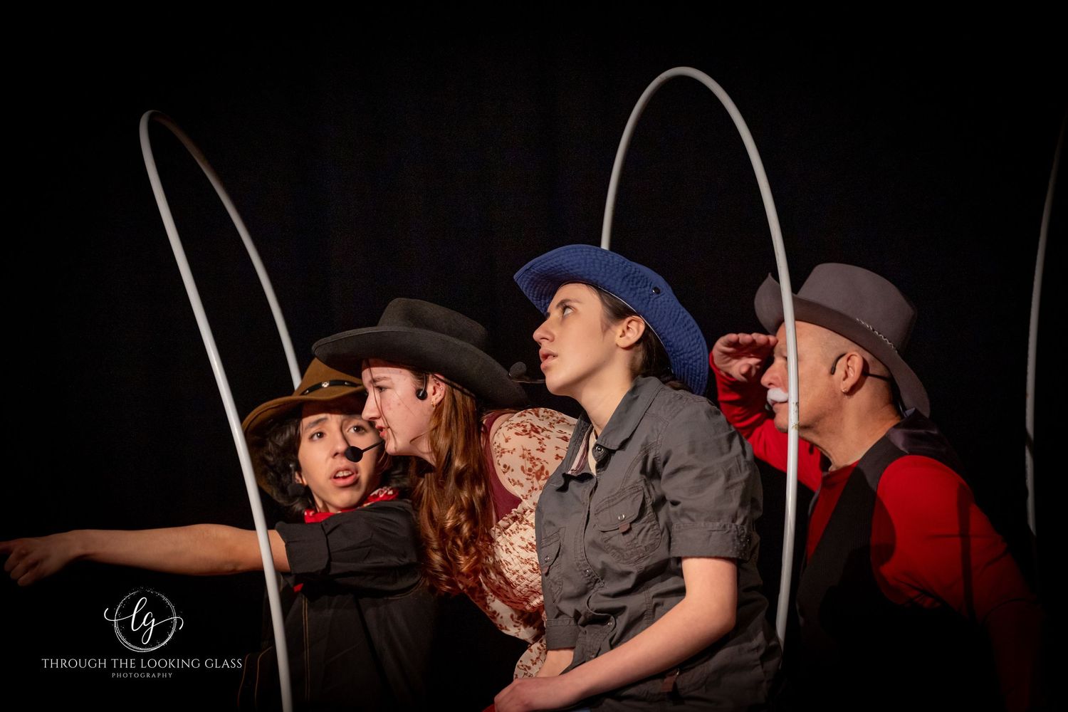 Group of performers in western attire lined up during theatrical production on dark stage.