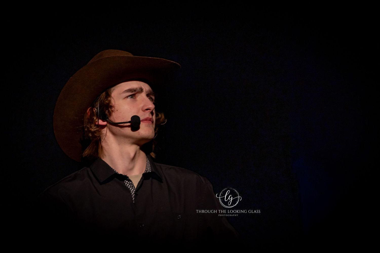 Actor in cowboy hat performs dramatic monologue against dark background.