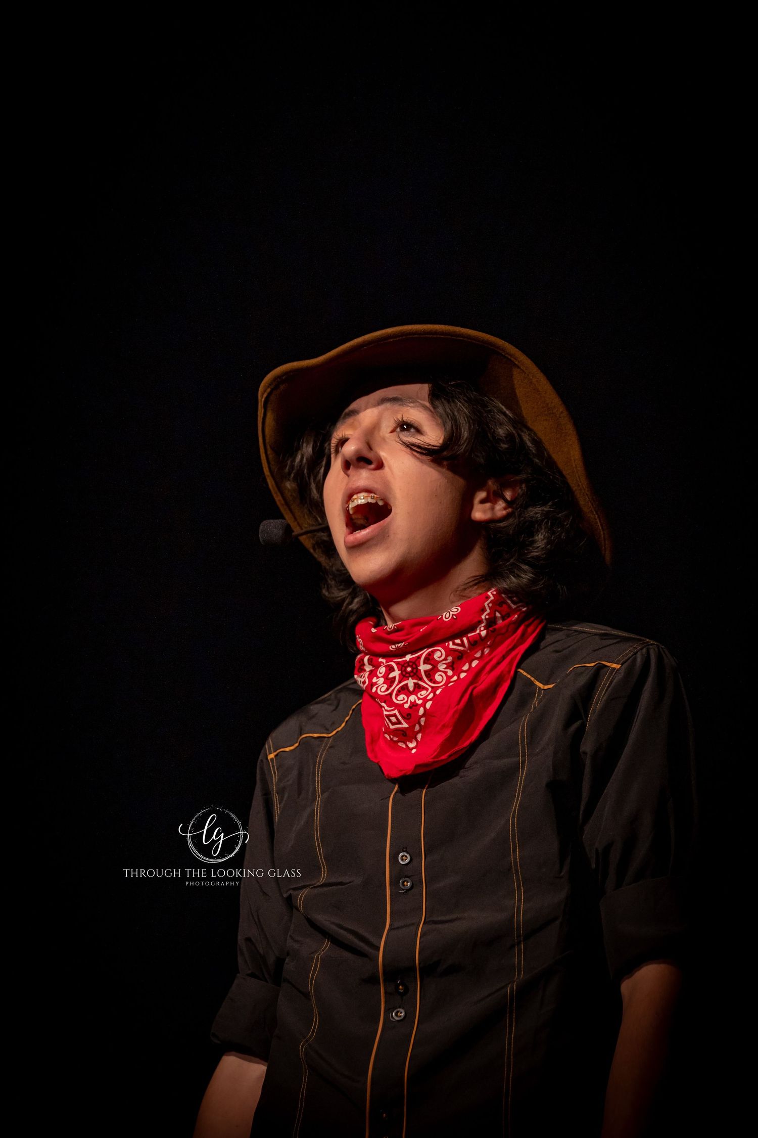 Dramatic portrait of performer in western wear with red bandana singing against dark background.