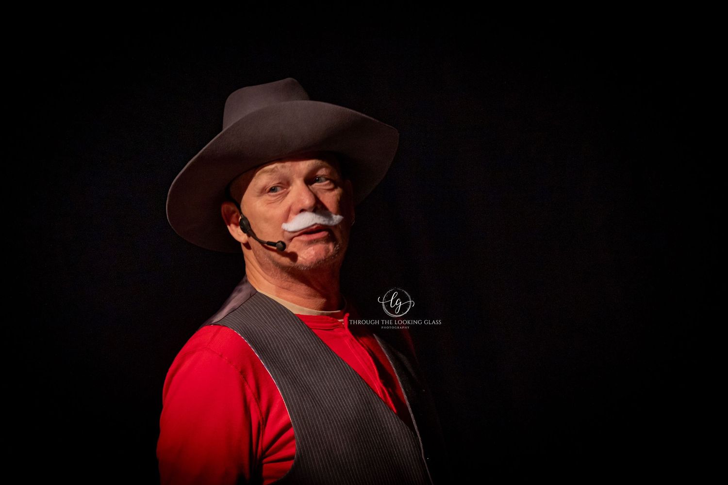 Portrait of western character with mustache wearing red shirt and brown vest against black background.