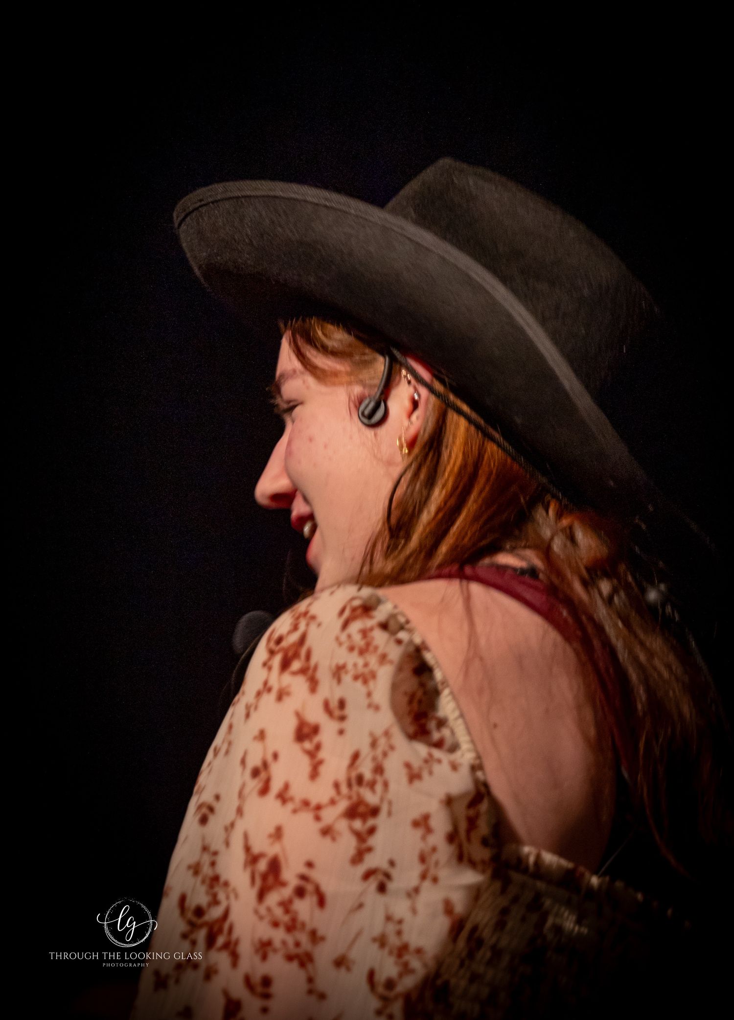 A performer in western attire with a cowboy hat laughs during a dramatic stage production.