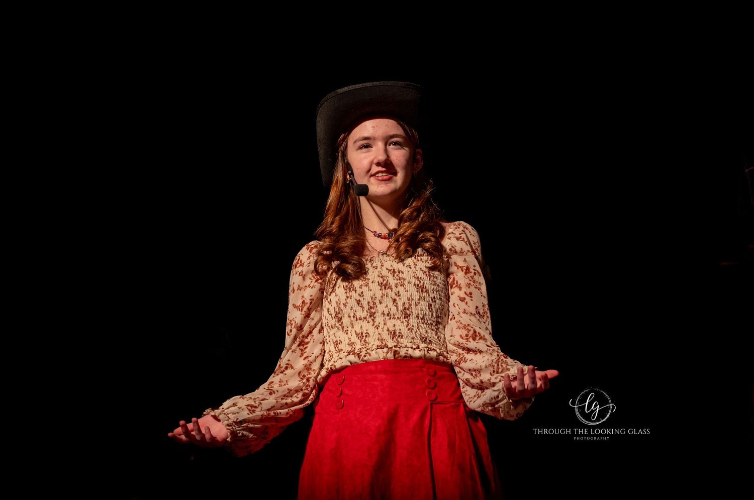 A performer in vintage clothing gestures expressively on a dark stage.