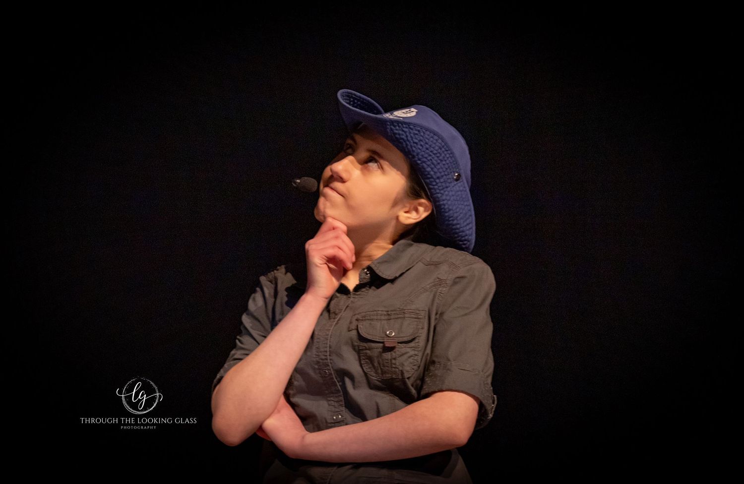 A contemplative performer in casual attire and baseball cap on a dark stage.