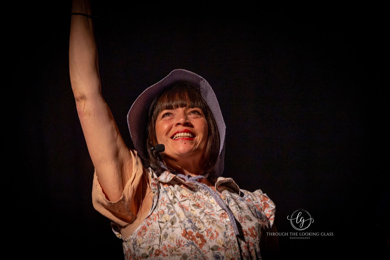 A joyful theatrical performer raises their arms in celebration on stage.
