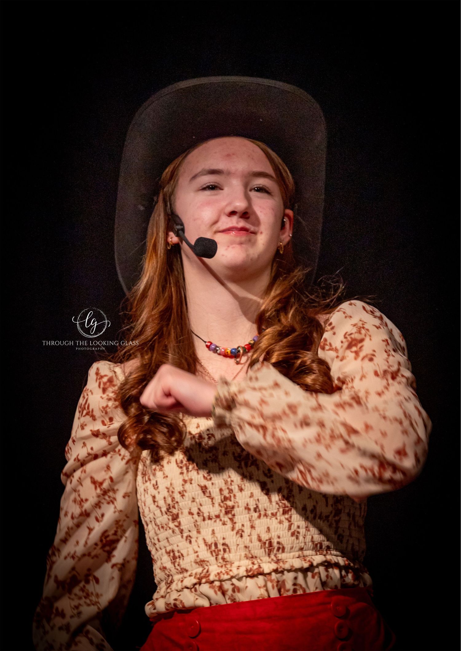 A performer in western attire and cowboy hat gestures dramatically during a stage show.