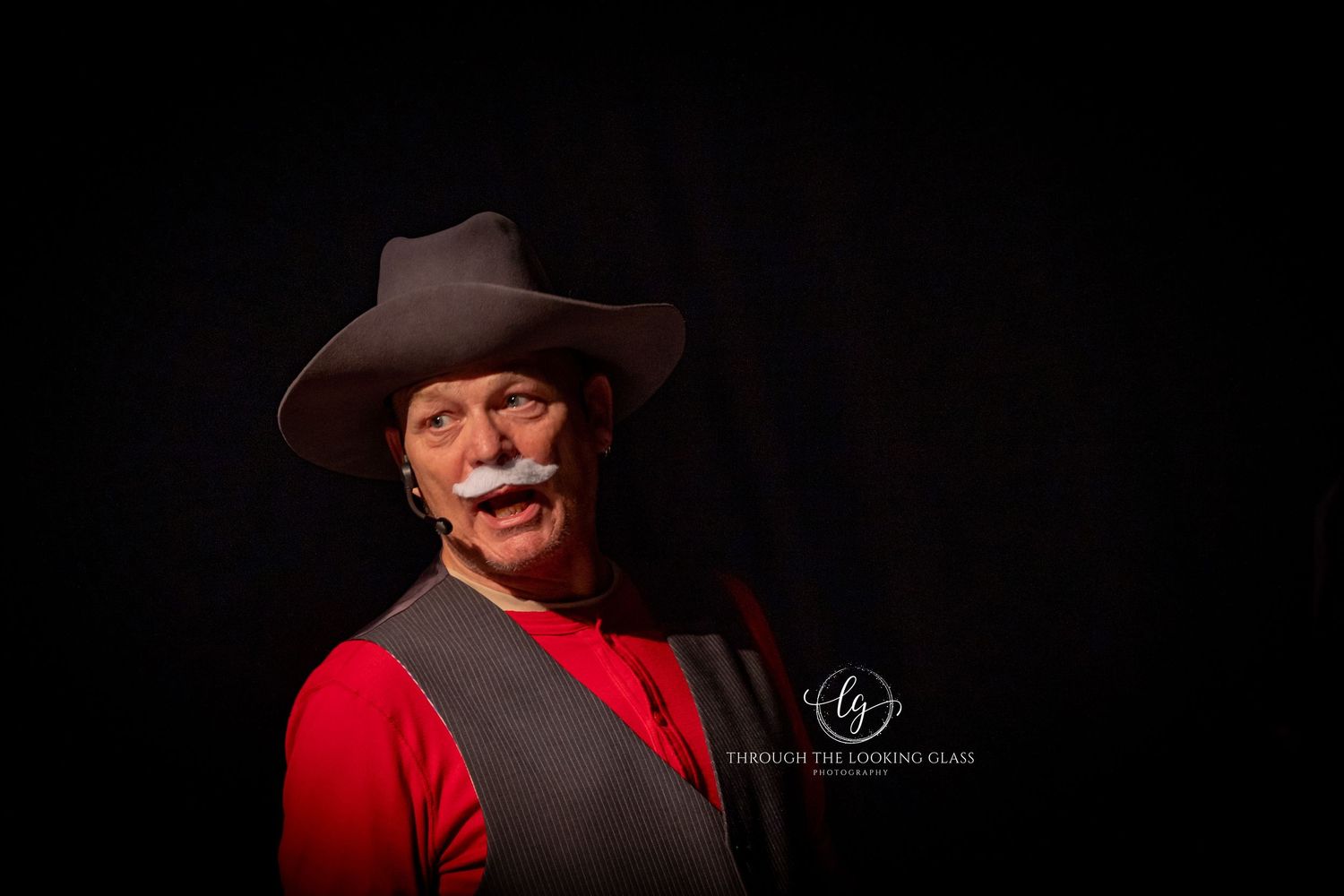 A performer in red and brown western attire smiles against a dark background.