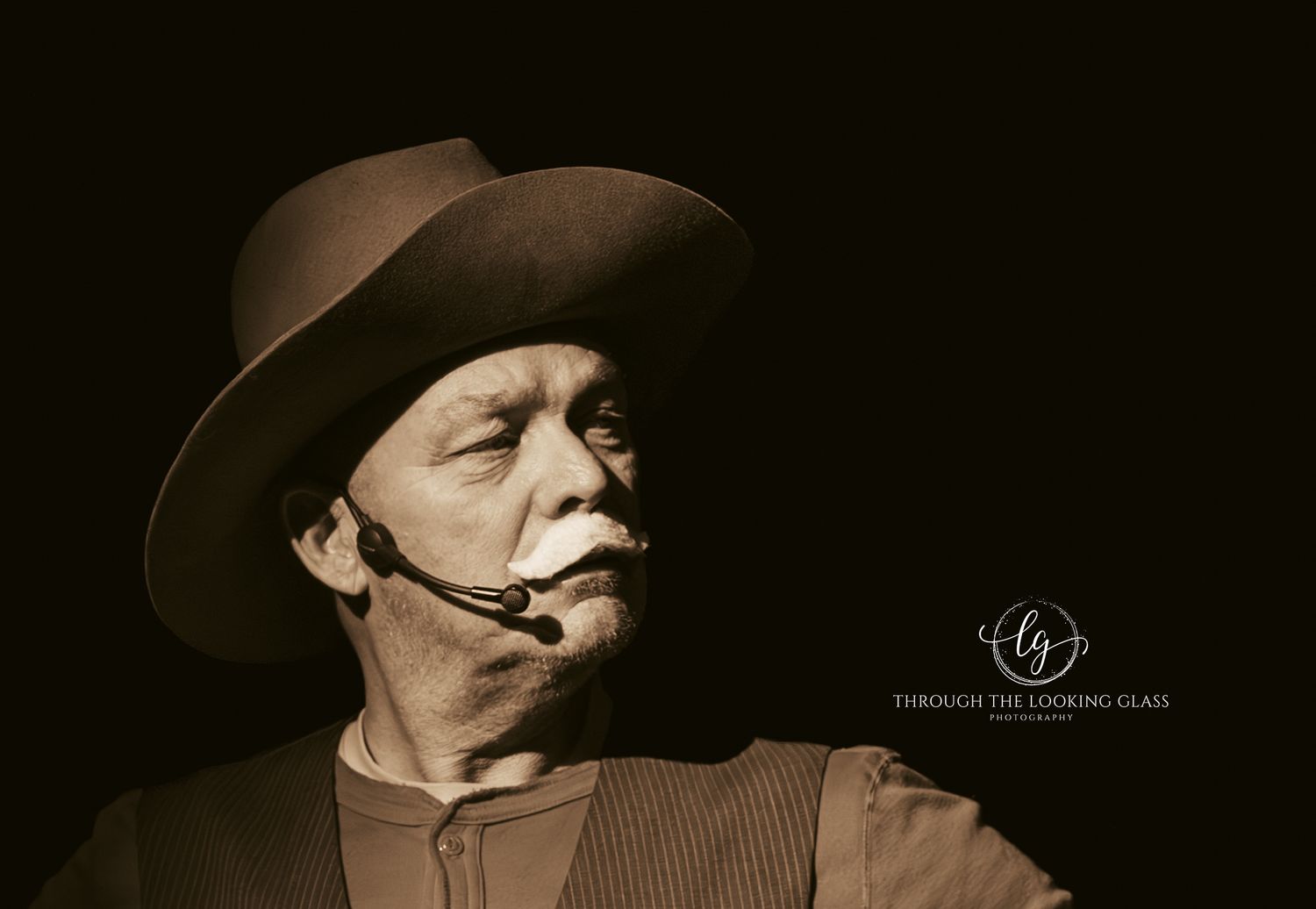 A performer in western attire with a cowboy hat delivers an intense dramatic moment on stage.