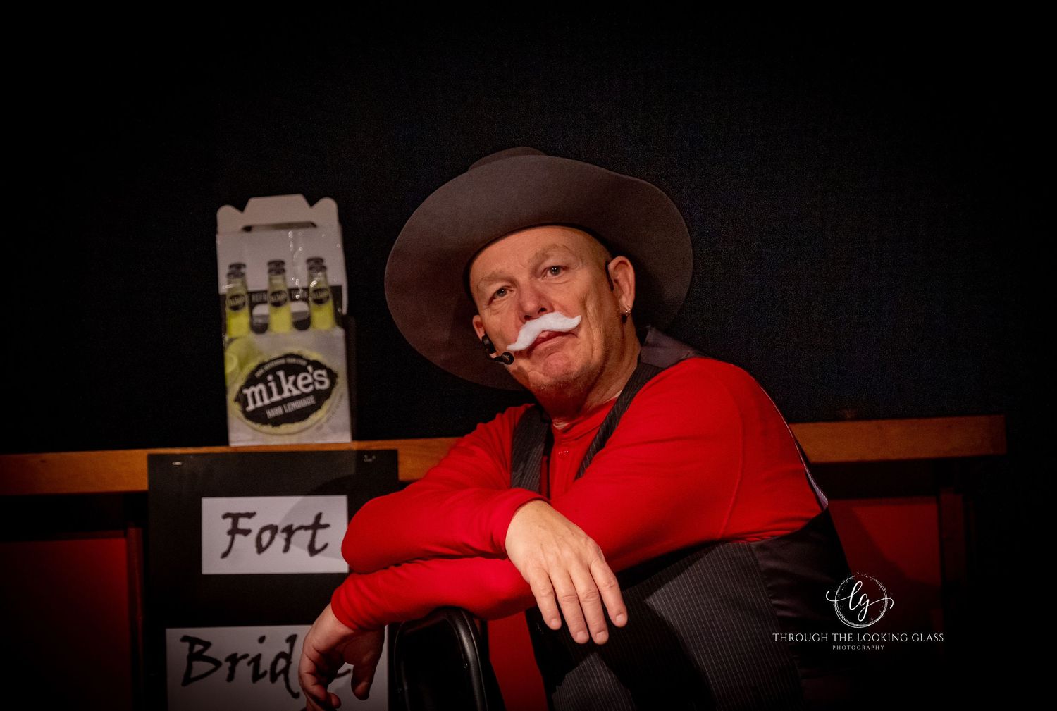 A costumed performer in western wear smiles warmly next to stage props.