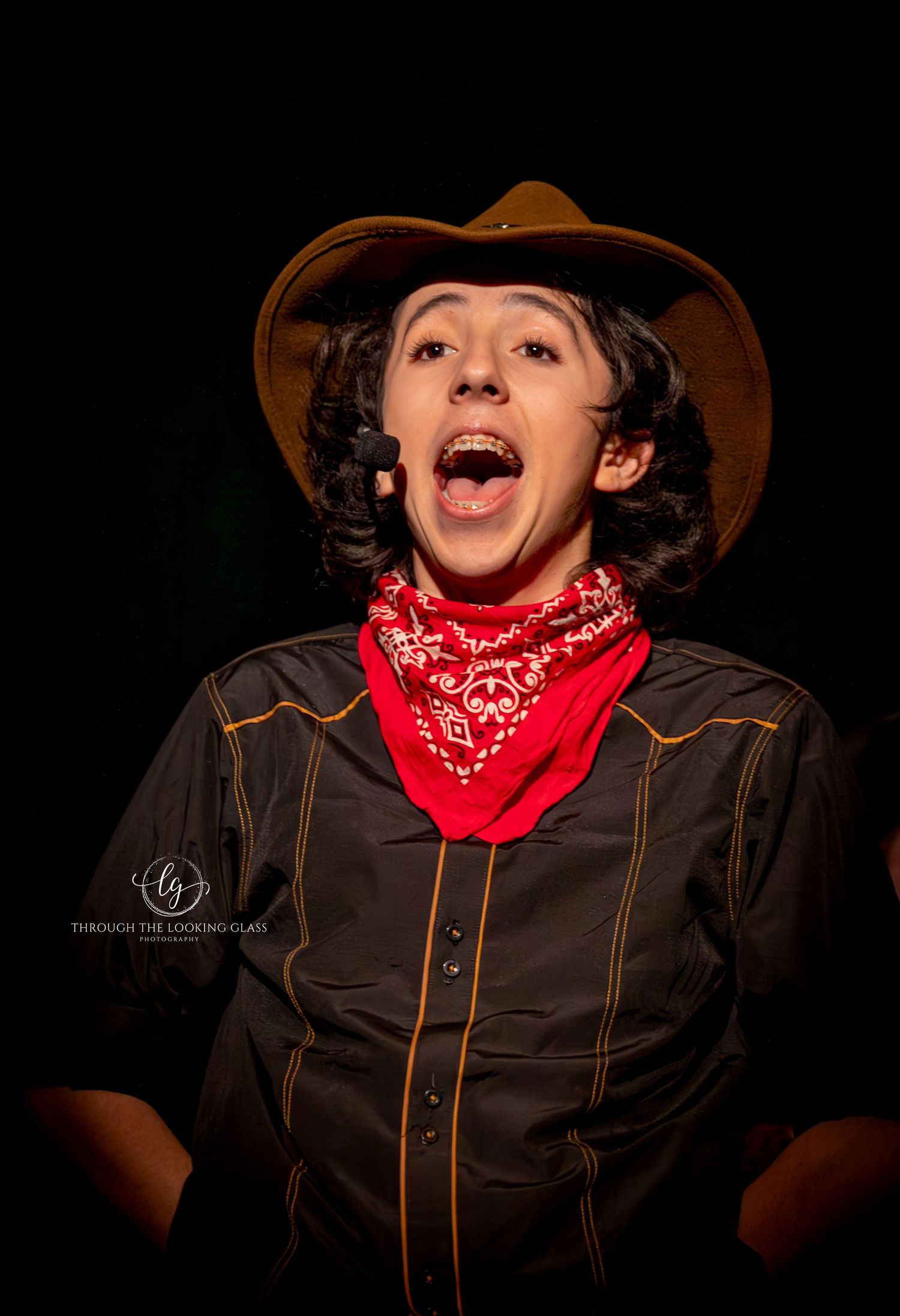 A theatrical performer in western costume with cowboy hat and bandana expresses joy during a show.