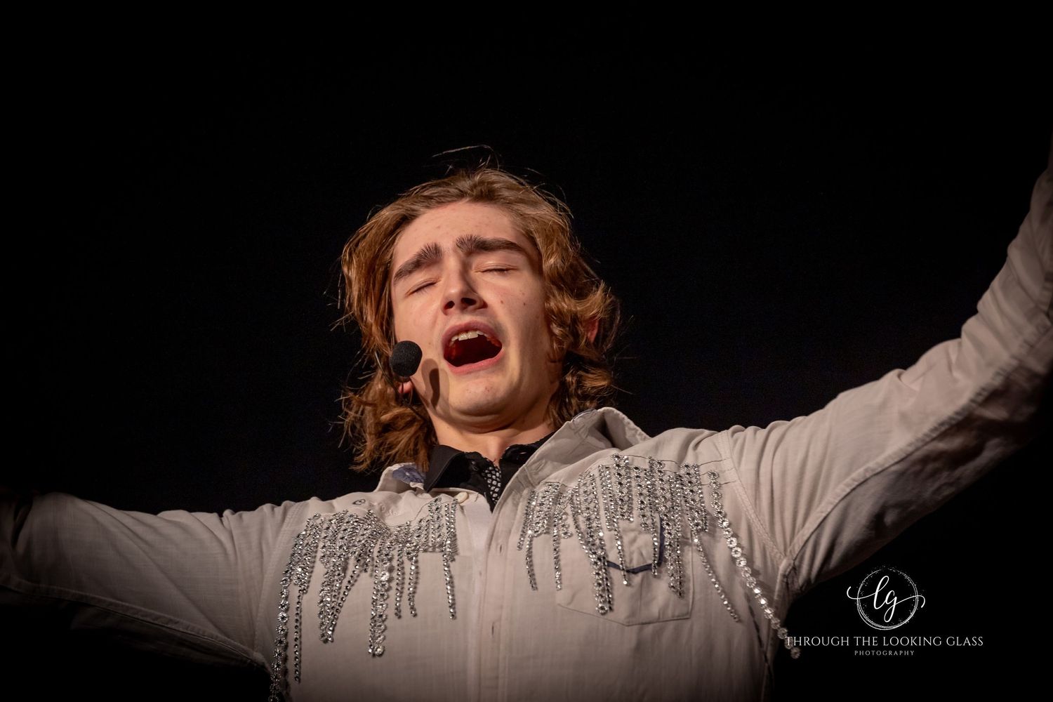 A dramatic performer in period costume passionately sings during a theatrical production.