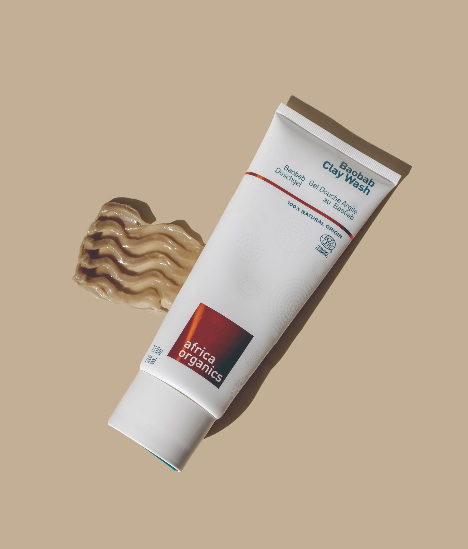 White cosmetic tube with swatches of brown product against beige background.