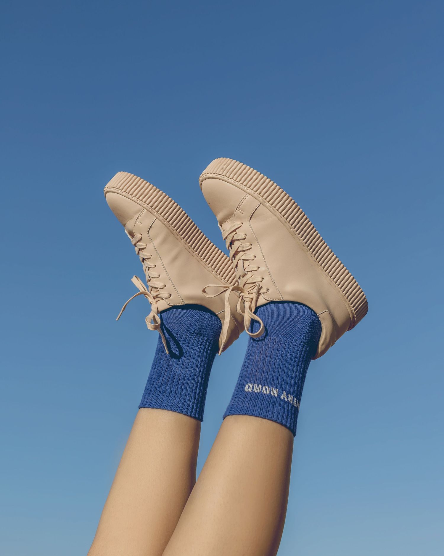 Beige sneakers and blue socks photographed against bright blue sky background.