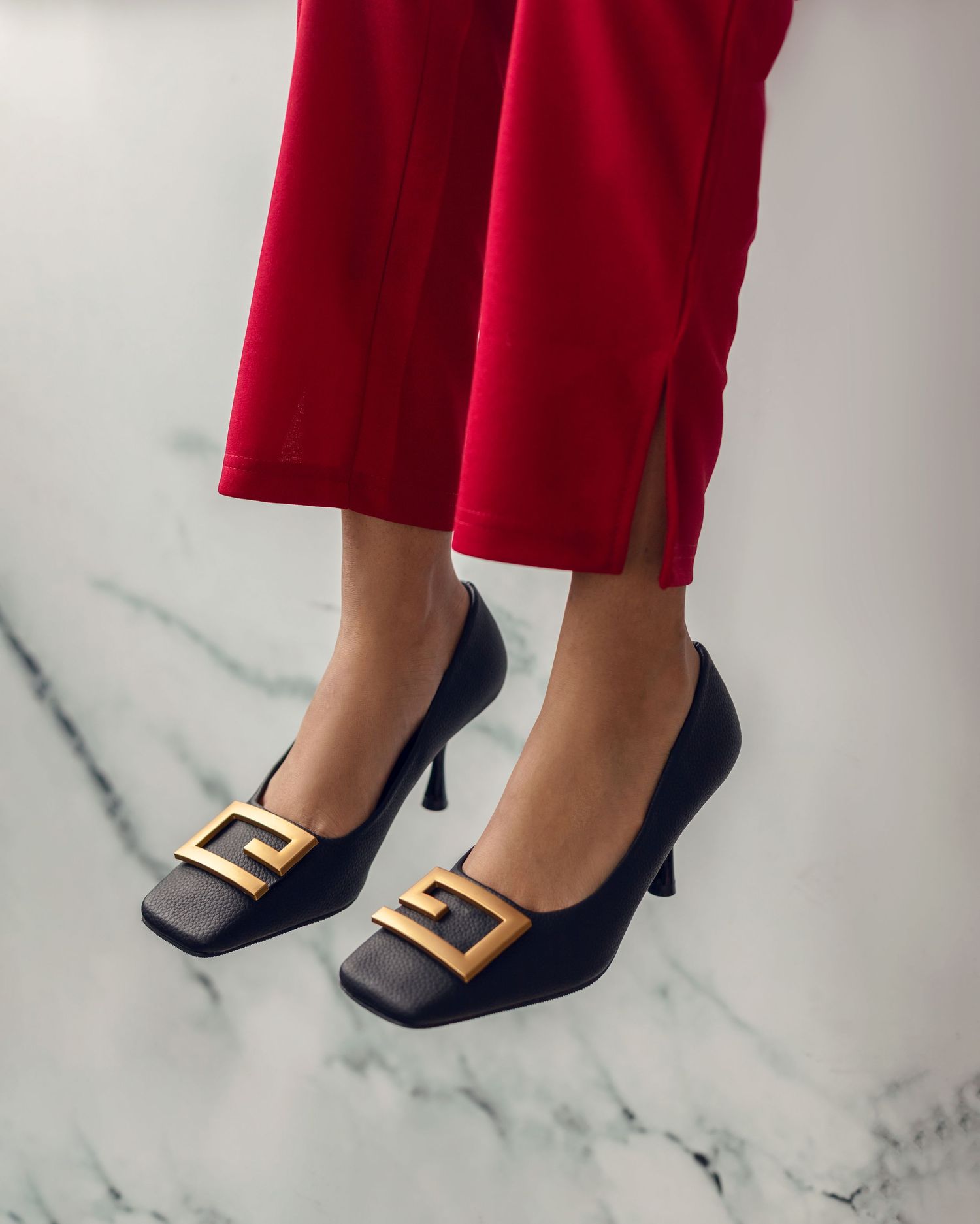 Navy blue suede pumps with gold buckle detail worn with red cropped pants.