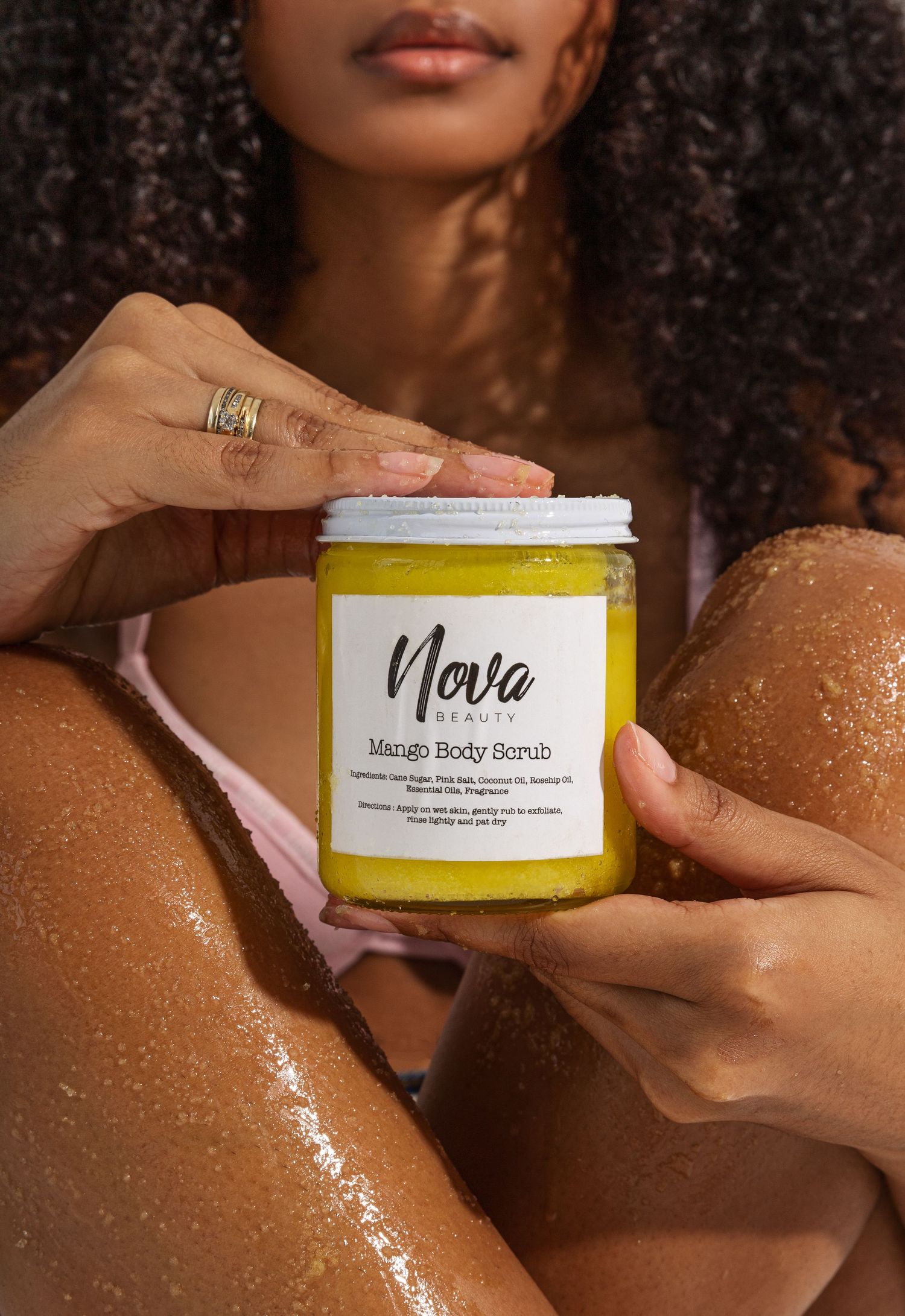 Yellow mango body scrub product jar held in hands with glowing skin.