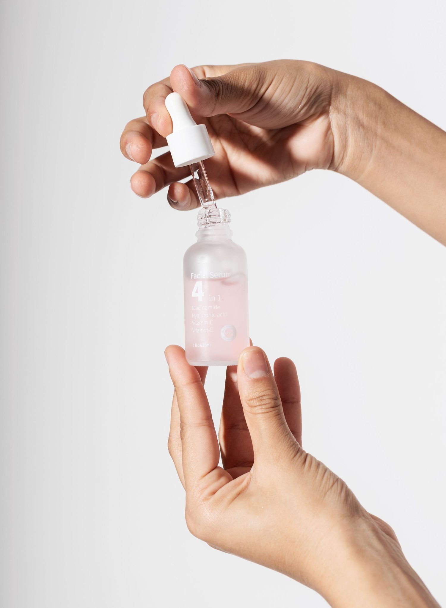 Hands holding a clear glass dropper bottle containing pink skincare serum.