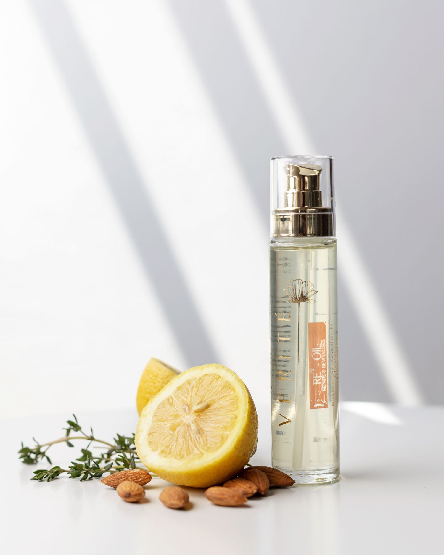 Perfume bottle with fresh lemon halves, herbs and almonds on white surface with dramatic shadows.