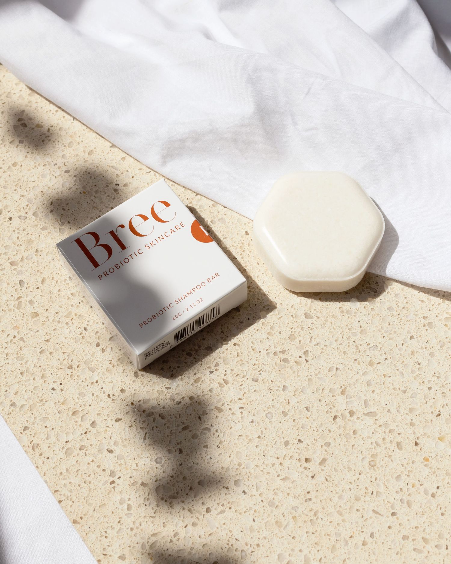 Brēe beauty product packaging and hexagonal soap bar on white fabric with shadows.