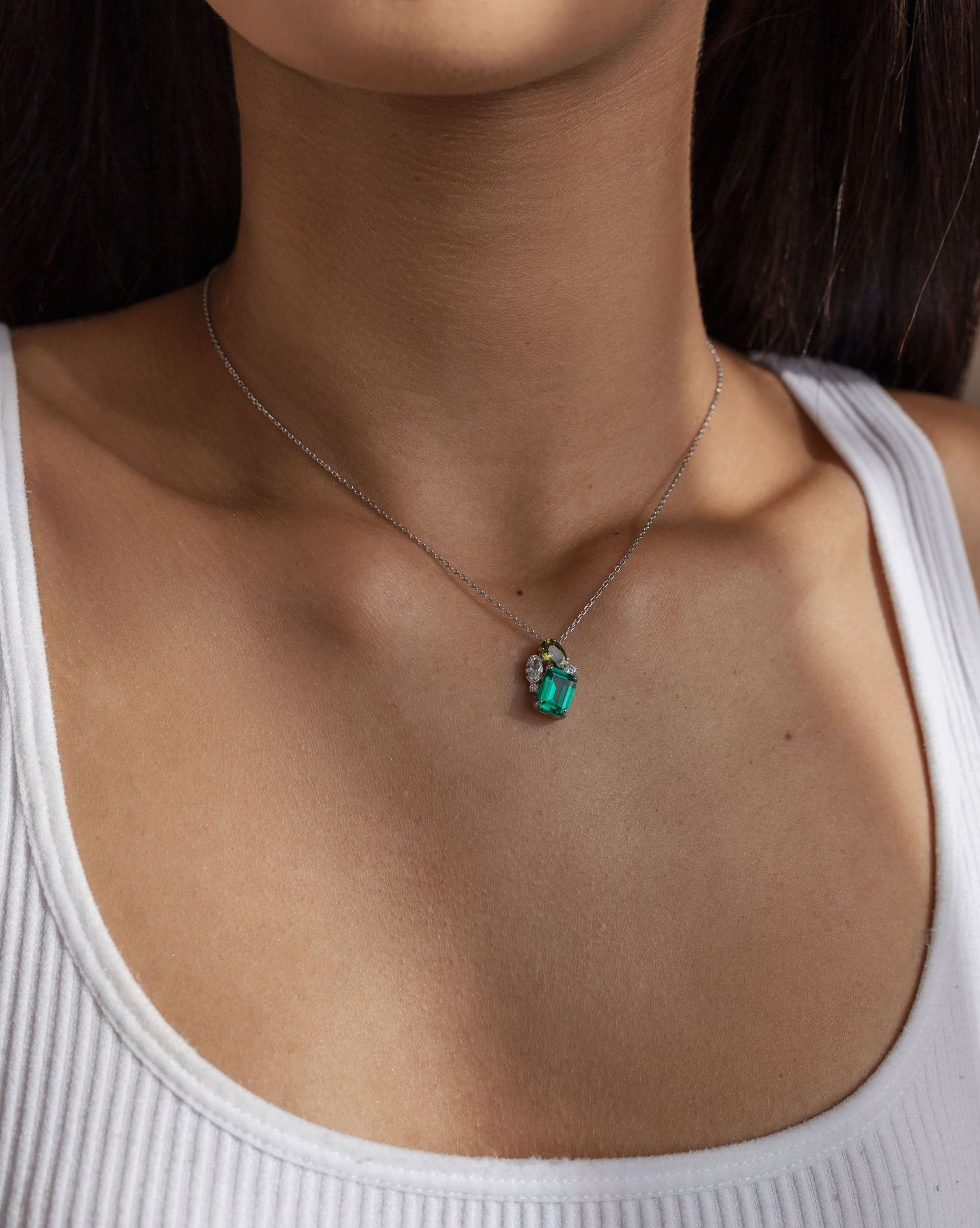 Dainty silver necklace featuring a striking emerald green pendant on a white tank top.
