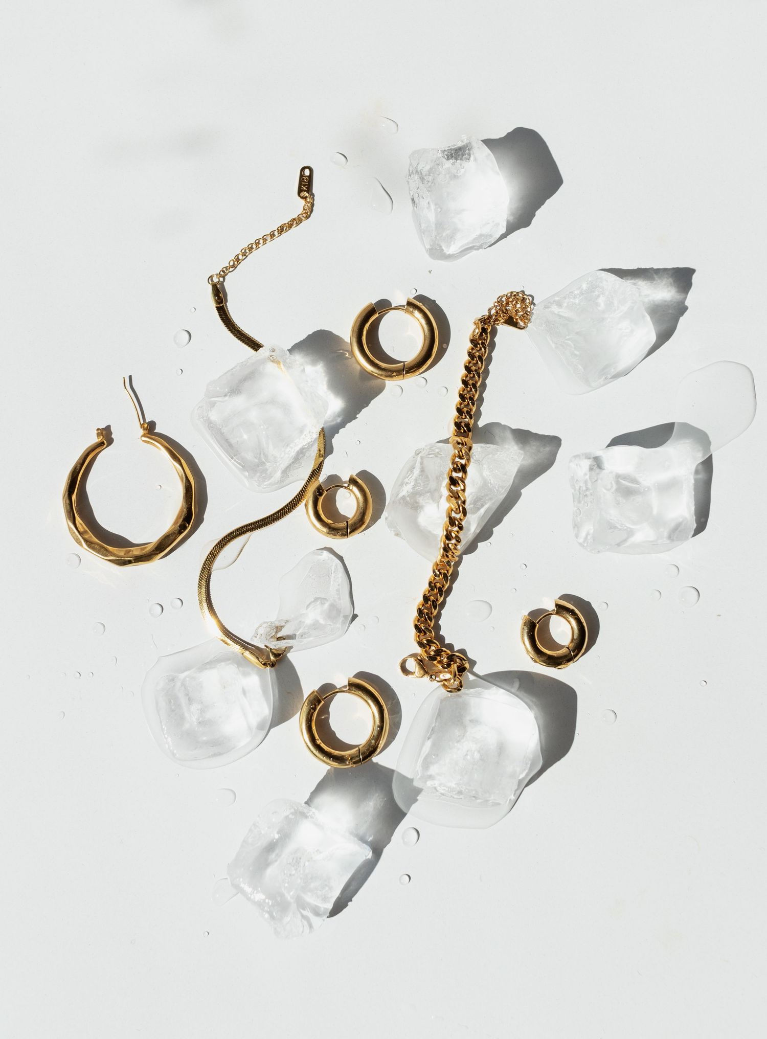 Gold jewelry rings and hoops arranged artistically with clear quartz crystals on white background.