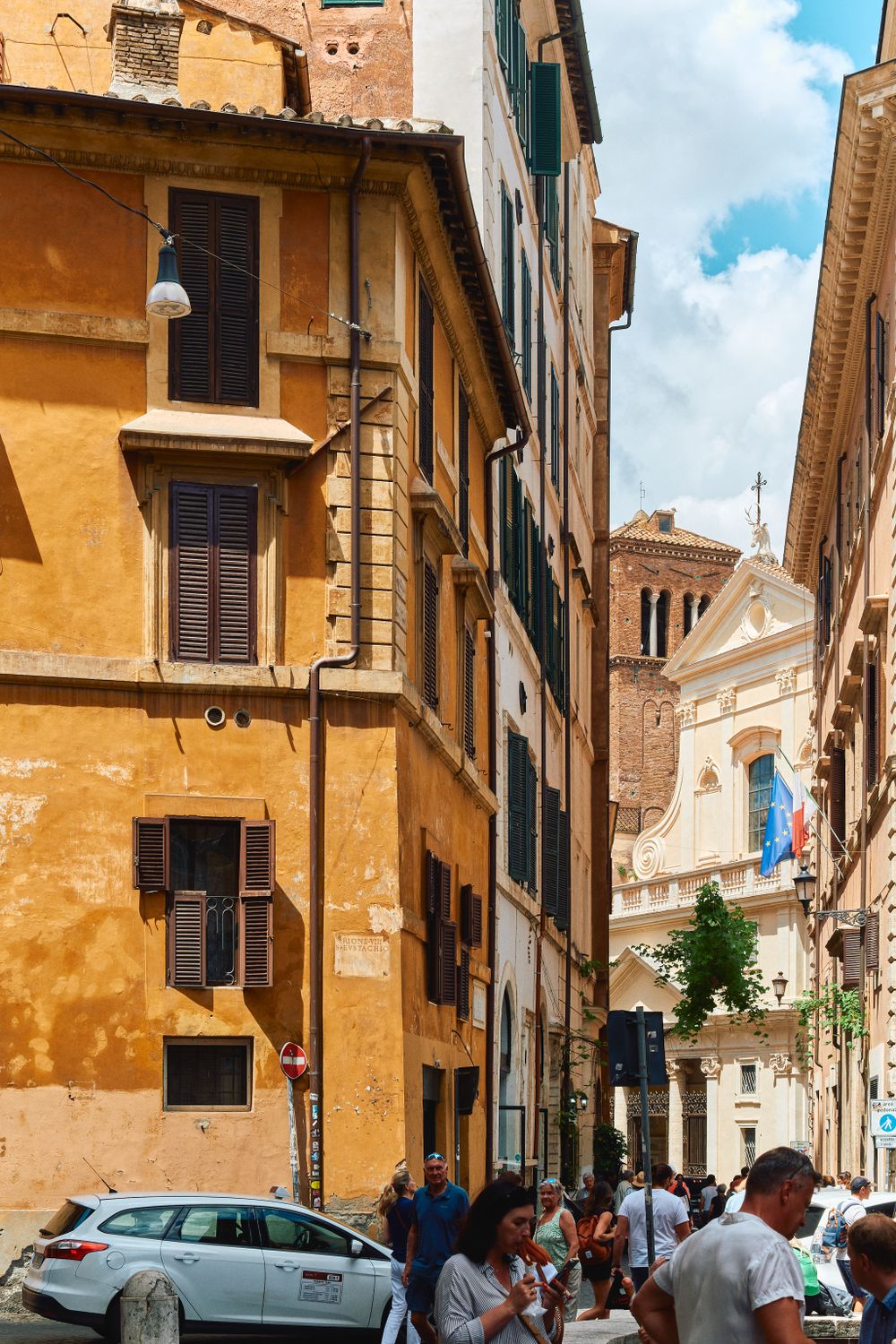 Narrow cobblestone street in Rome with ochre buildings leading to historic church facade.
