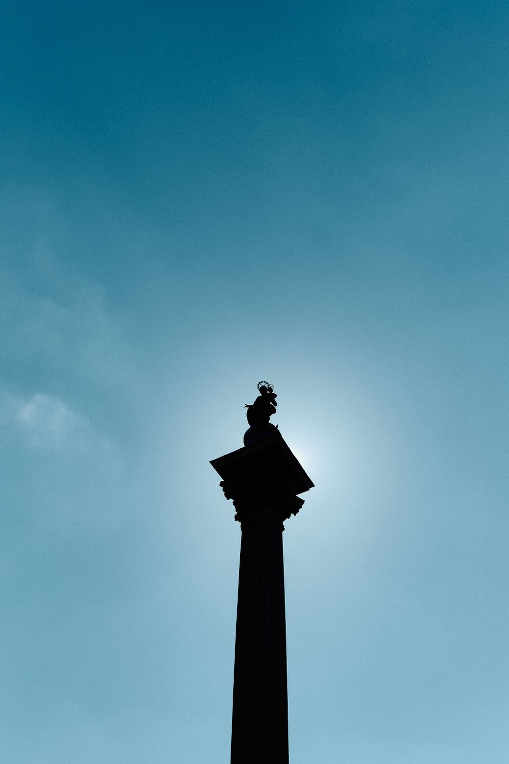 Silhouette of a monument column against bright blue sky with dramatic backlighting.