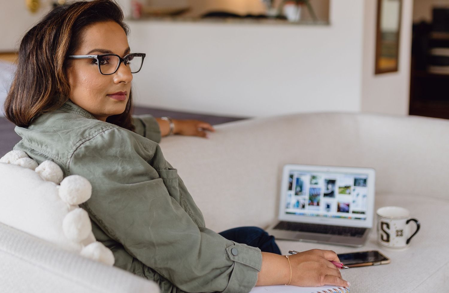 A woman sits looking out a window with a notepad, laptop, mug during an influencer branding photoshoot in Kansas City.