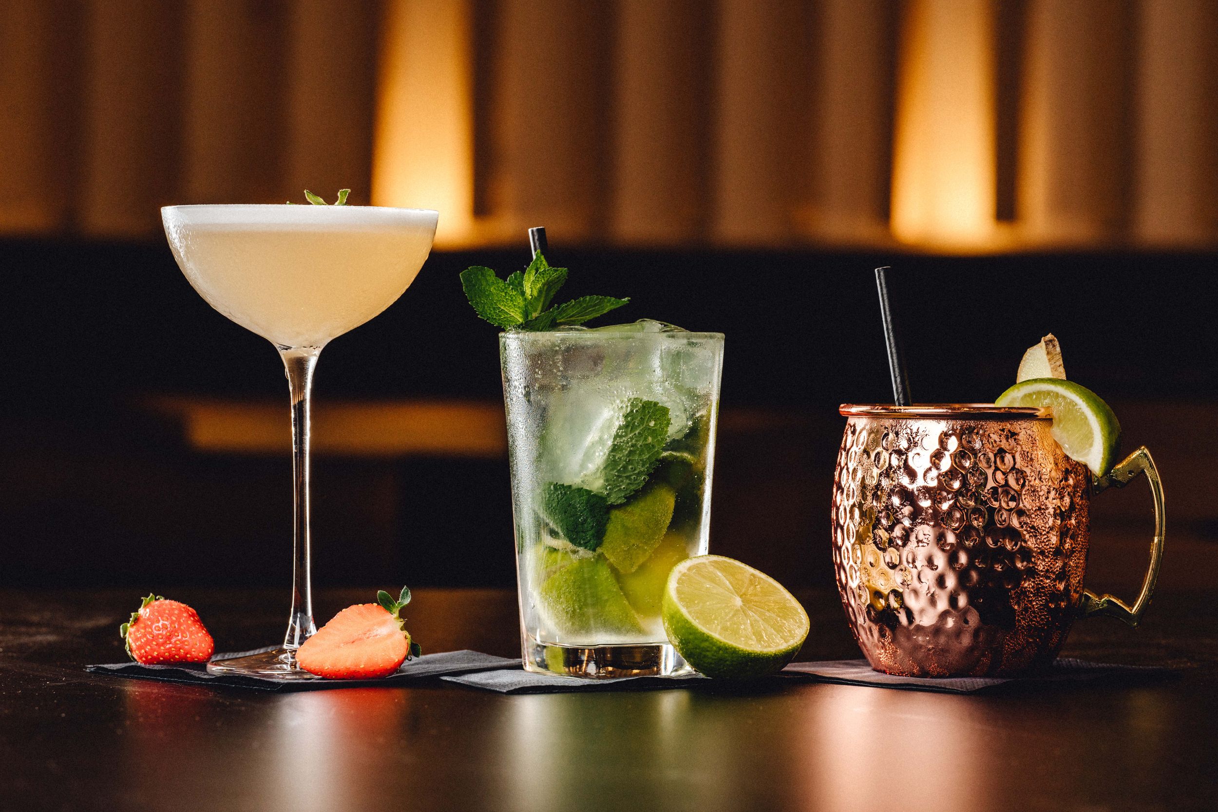 Illuminated bar setting with various cocktails and garnishes in elegant glassware.
