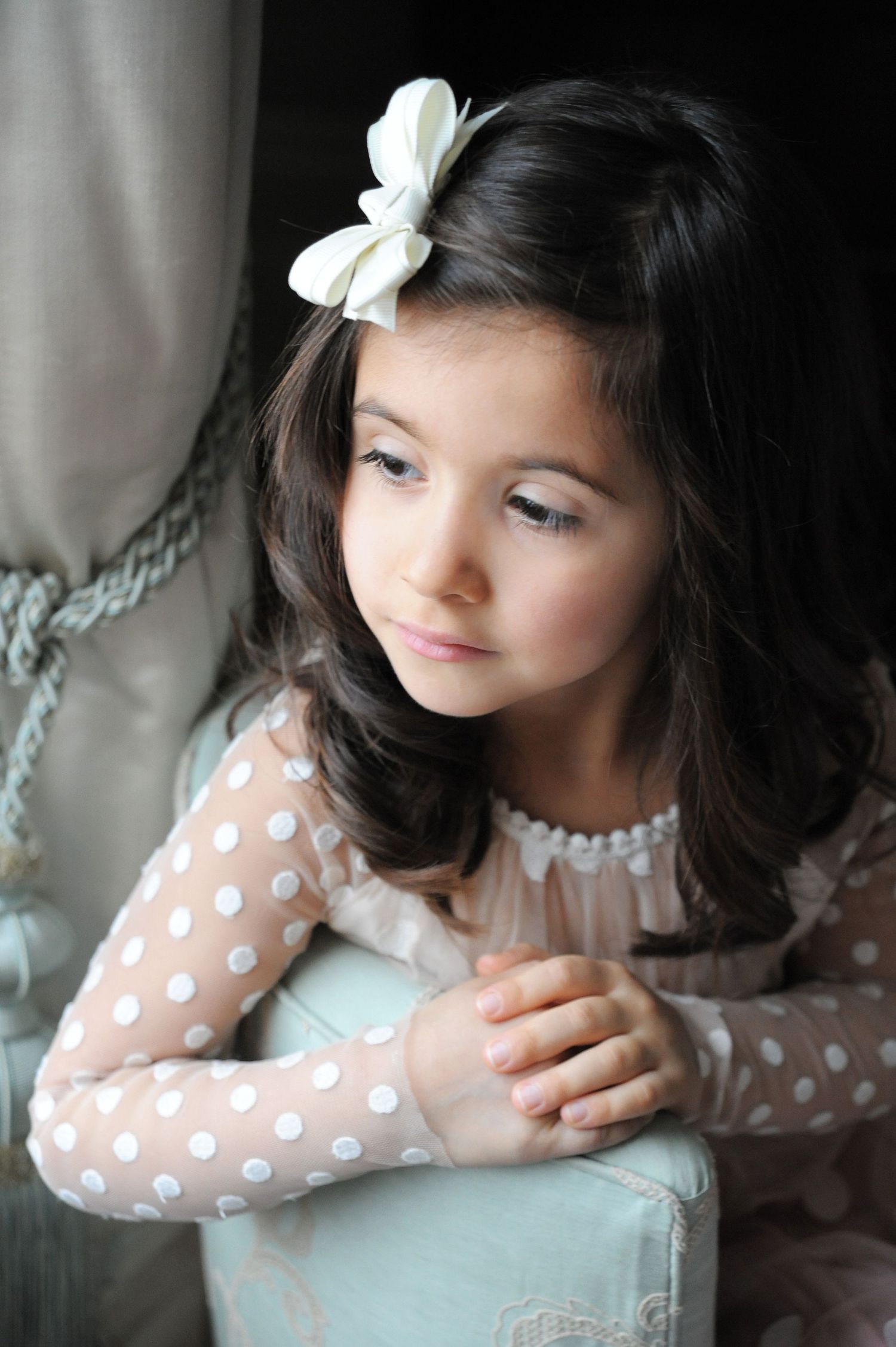 Portrait of a child in a polka dot dress with white bow hair accessory.