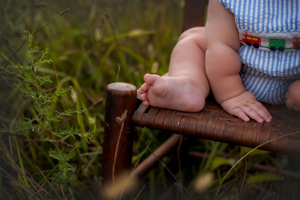 Six month old baby boy's foot and chubby hand on the edge of the chair.