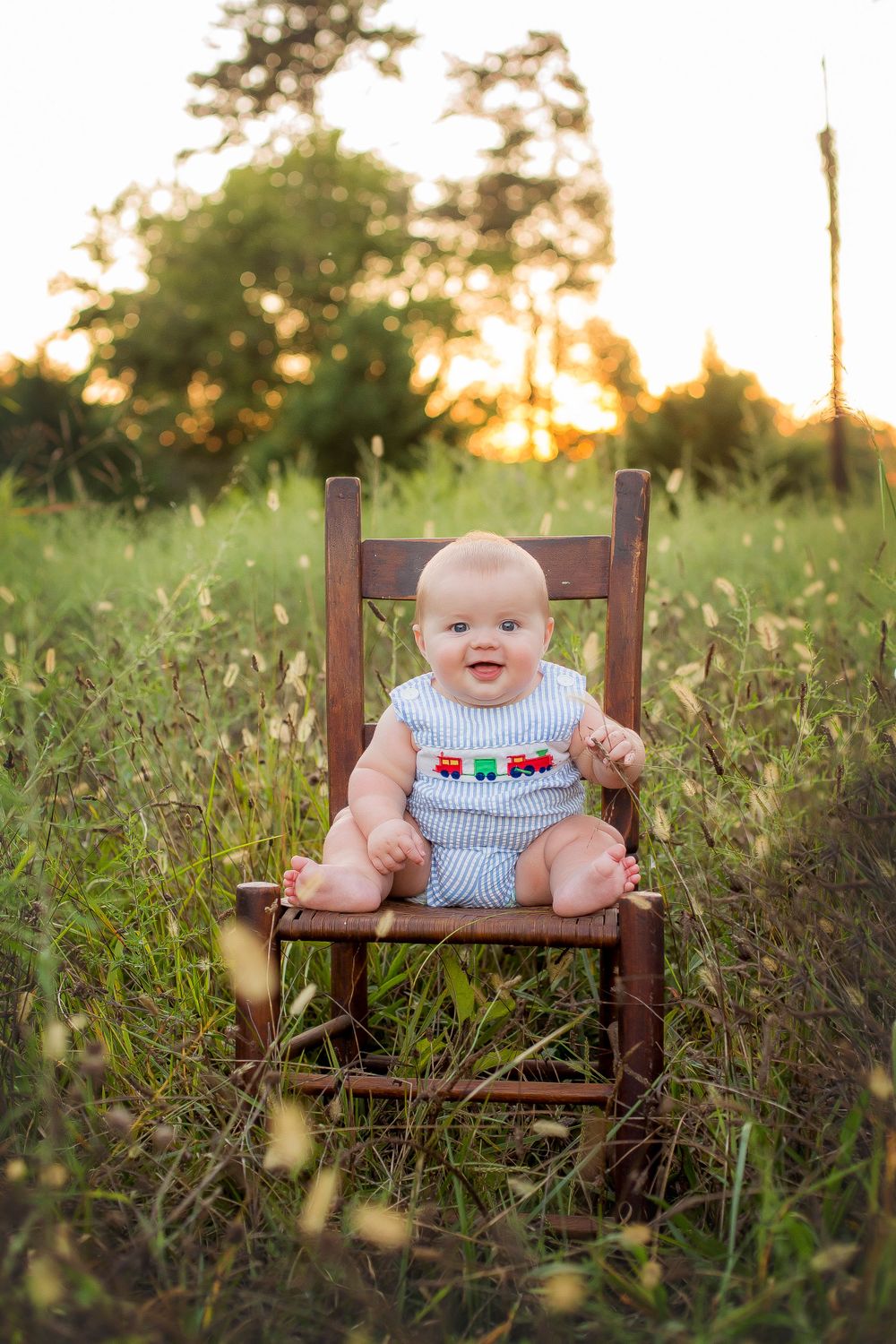 Six month old baby boy sitting on a chair in a field at sunset.