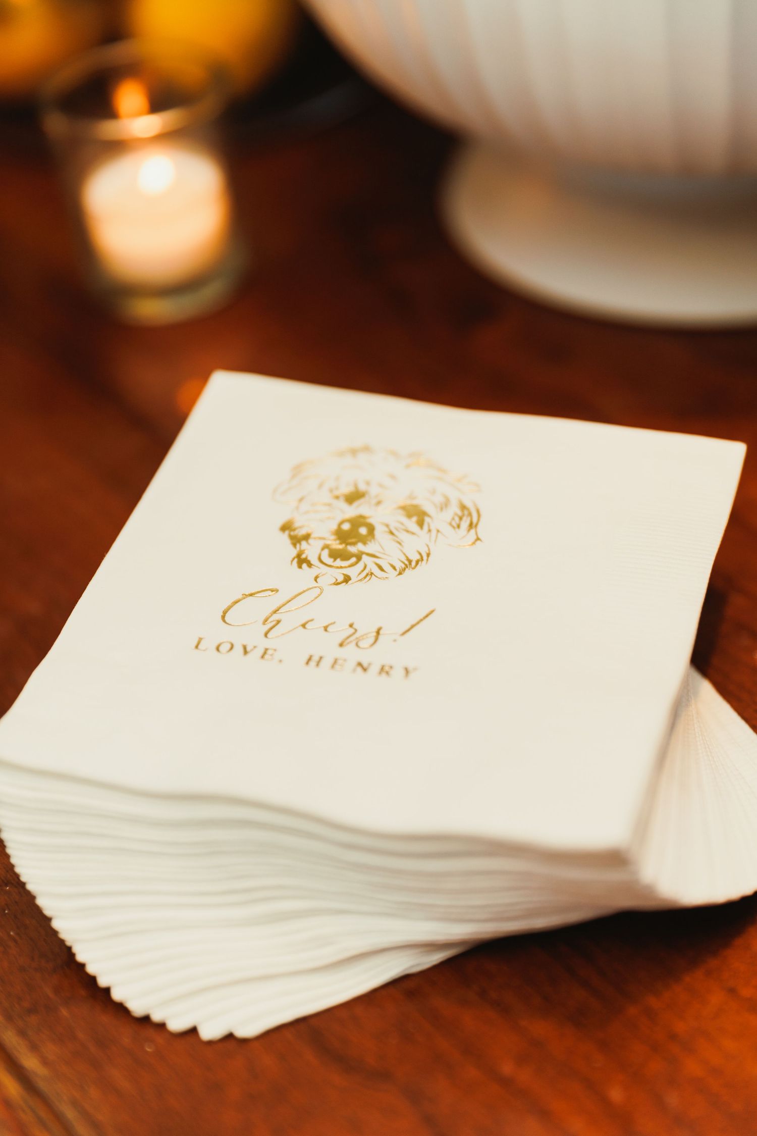 White wedding napkins with elegant gold monogram text stacked on dark wooden surface.