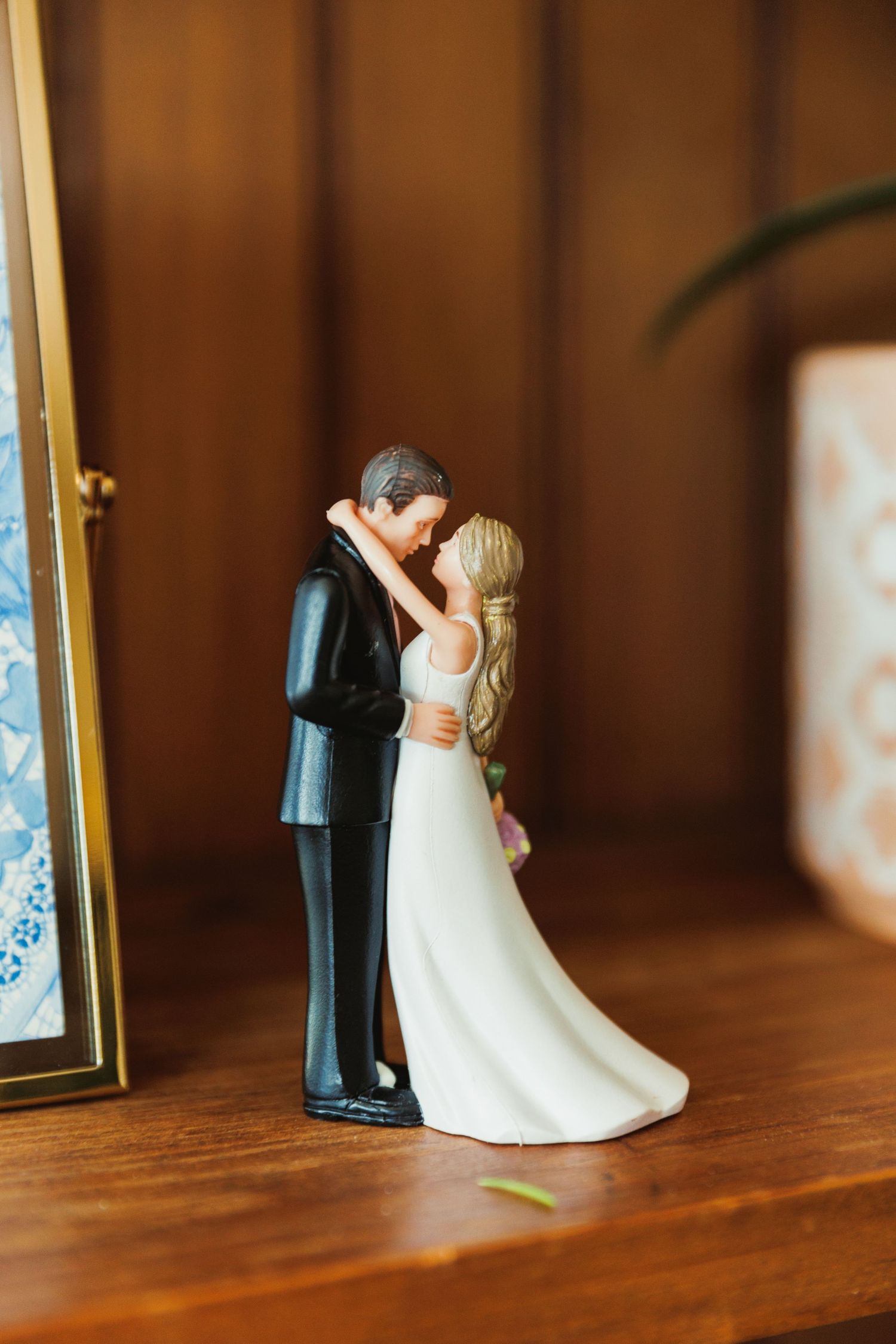 Small decorative bride and groom cake toppers displayed on wooden shelf.