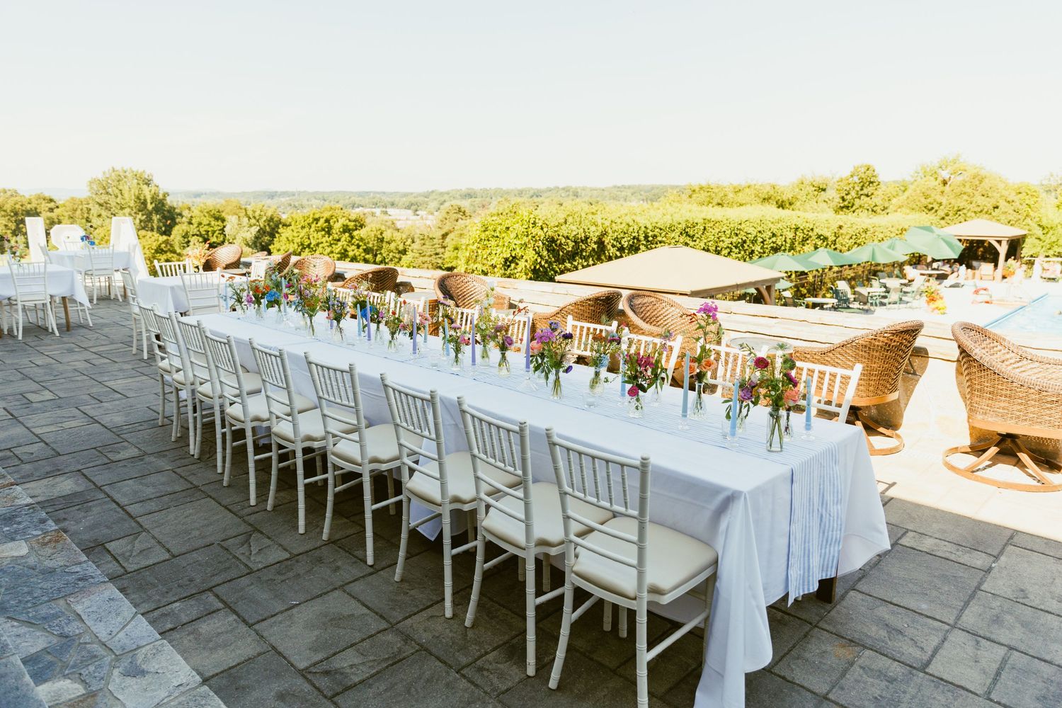 Long white reception tables and chairs set up outdoors for an elegant wedding celebration.