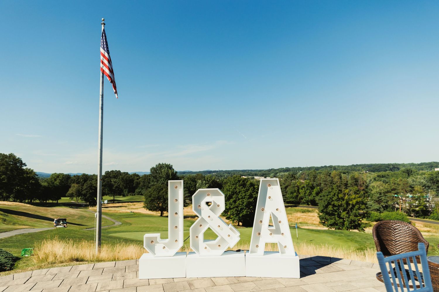 Outdoor wedding venue setup with American flag against clear blue sky.