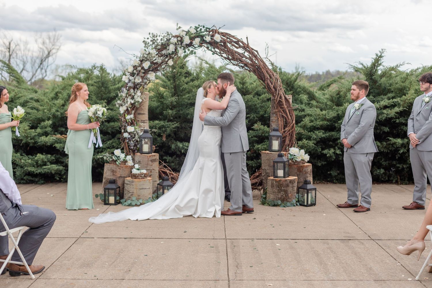 Wedding ceremony in progress under a floral arch with bridesmaids in mint green dresses.