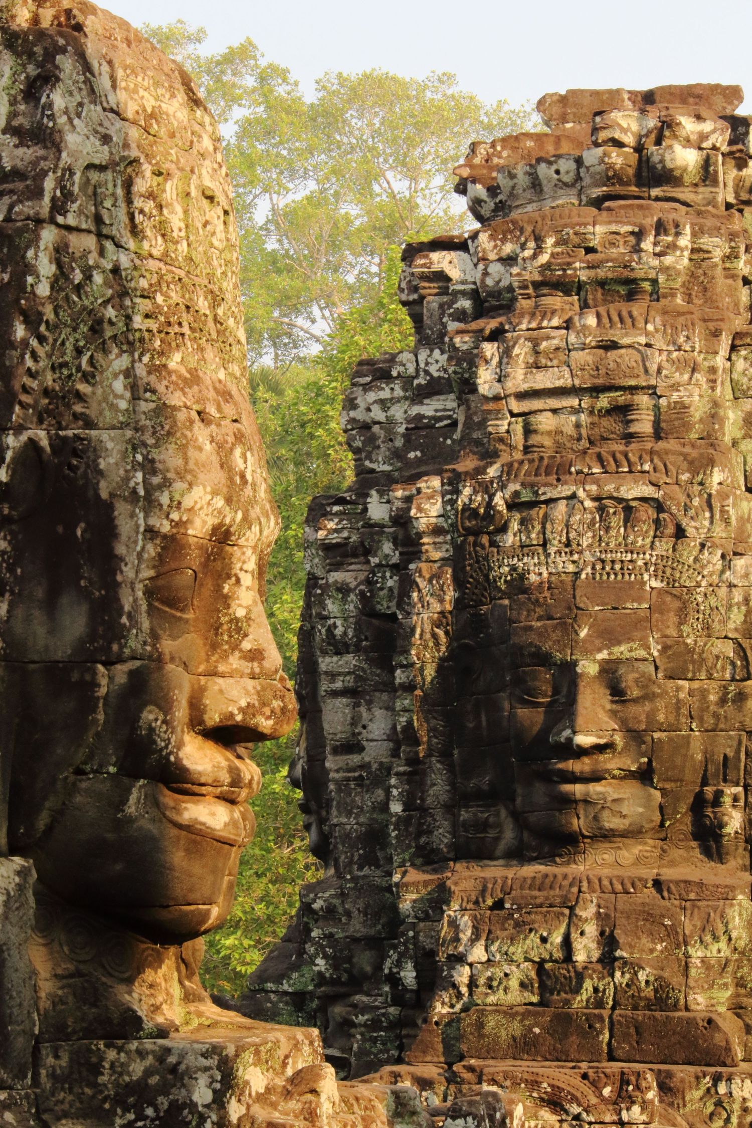 Giant stone faces carved into Bayon temple towers catch golden sunlight in Angkor.
