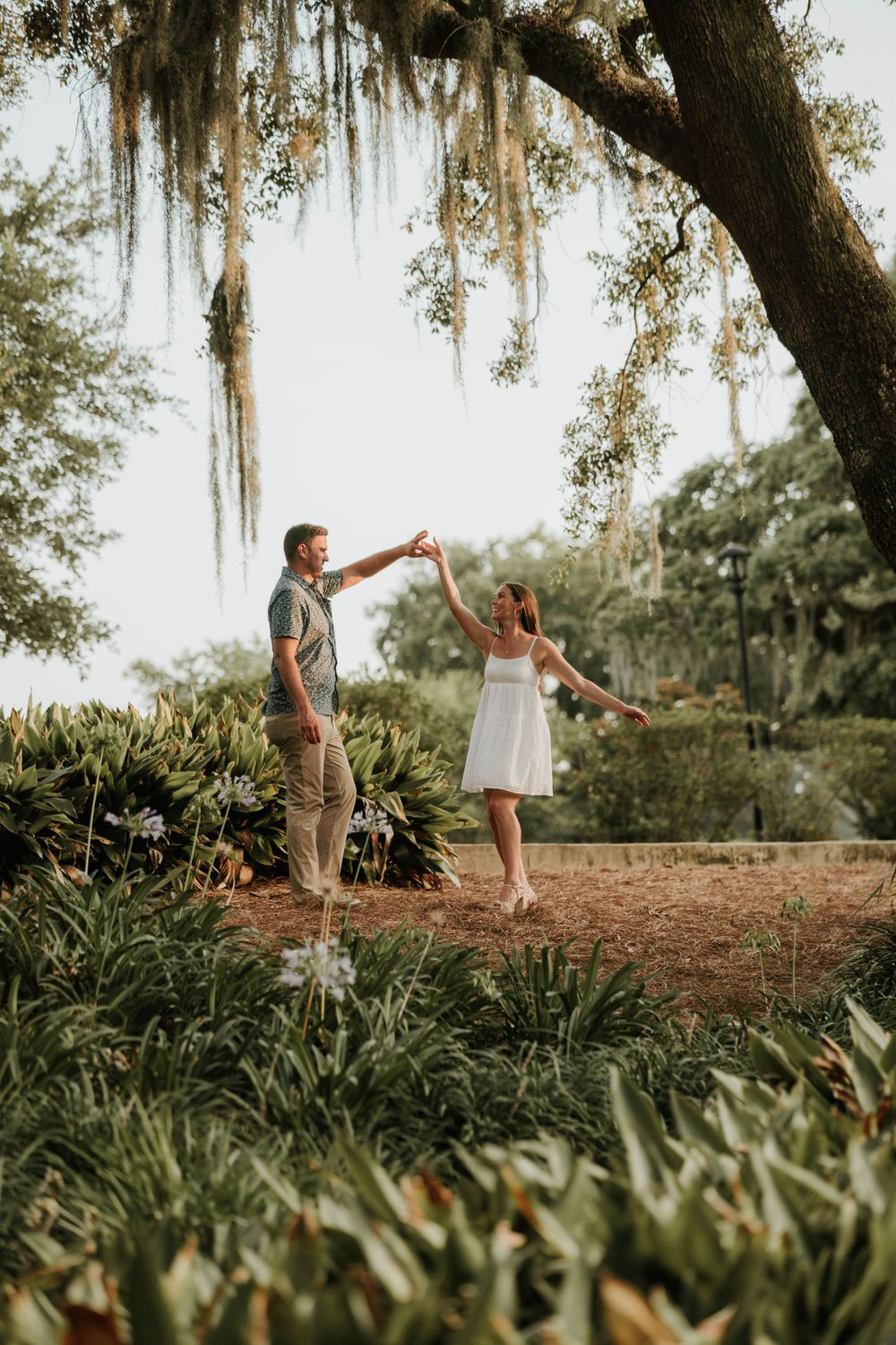Couple dancing under Spanish moss draped oak tree in garden setting.
