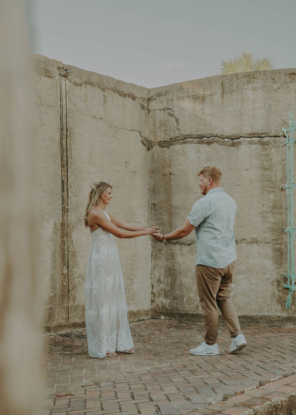 Couple in formal attire dancing in an outdoor courtyard with concrete walls.