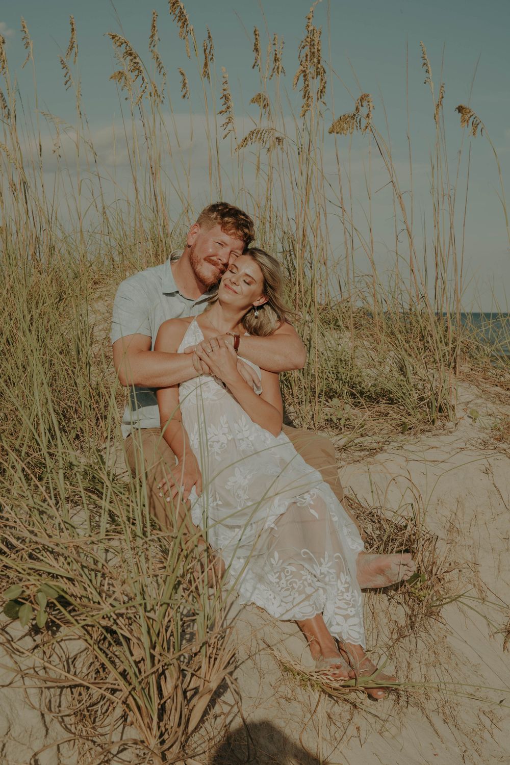 Intimate beach portrait showing couple cuddling among coastal dune grass.