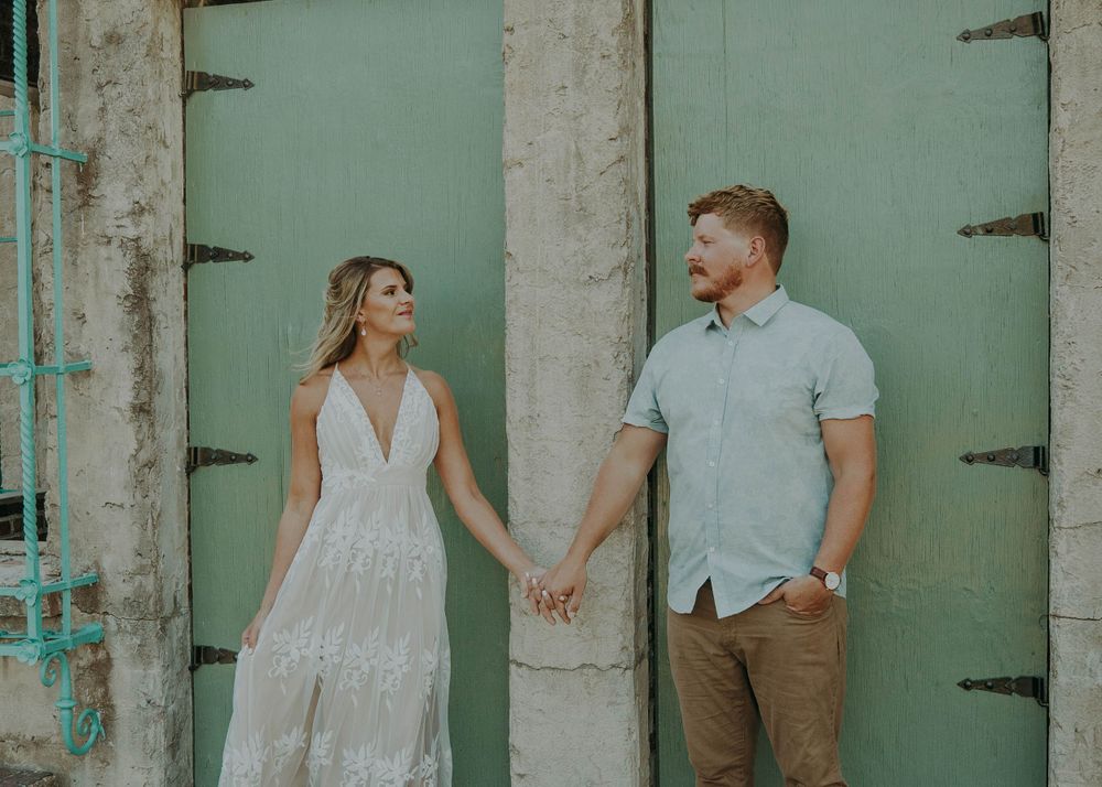 A couple holds hands while standing between mint green doors during an outdoor photoshoot.