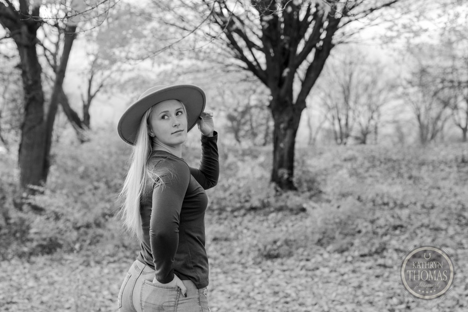 Black and white portrait featuring casual autumn attire and wide brim hat in a wooded setting.