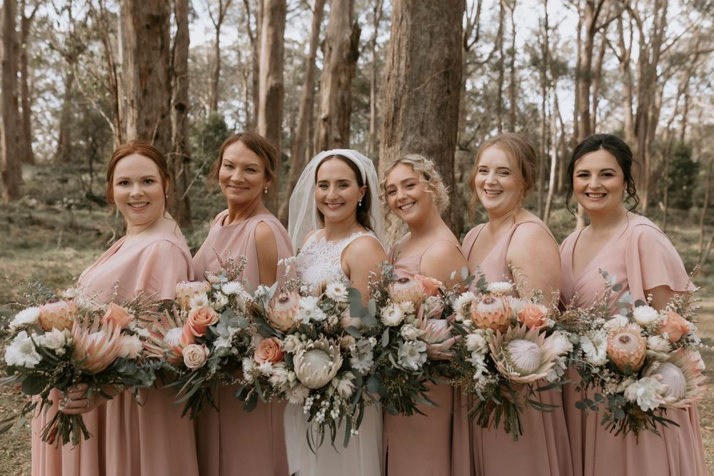 Bridesmaids in pink dresses hold elegant floral bouquets while posing together.