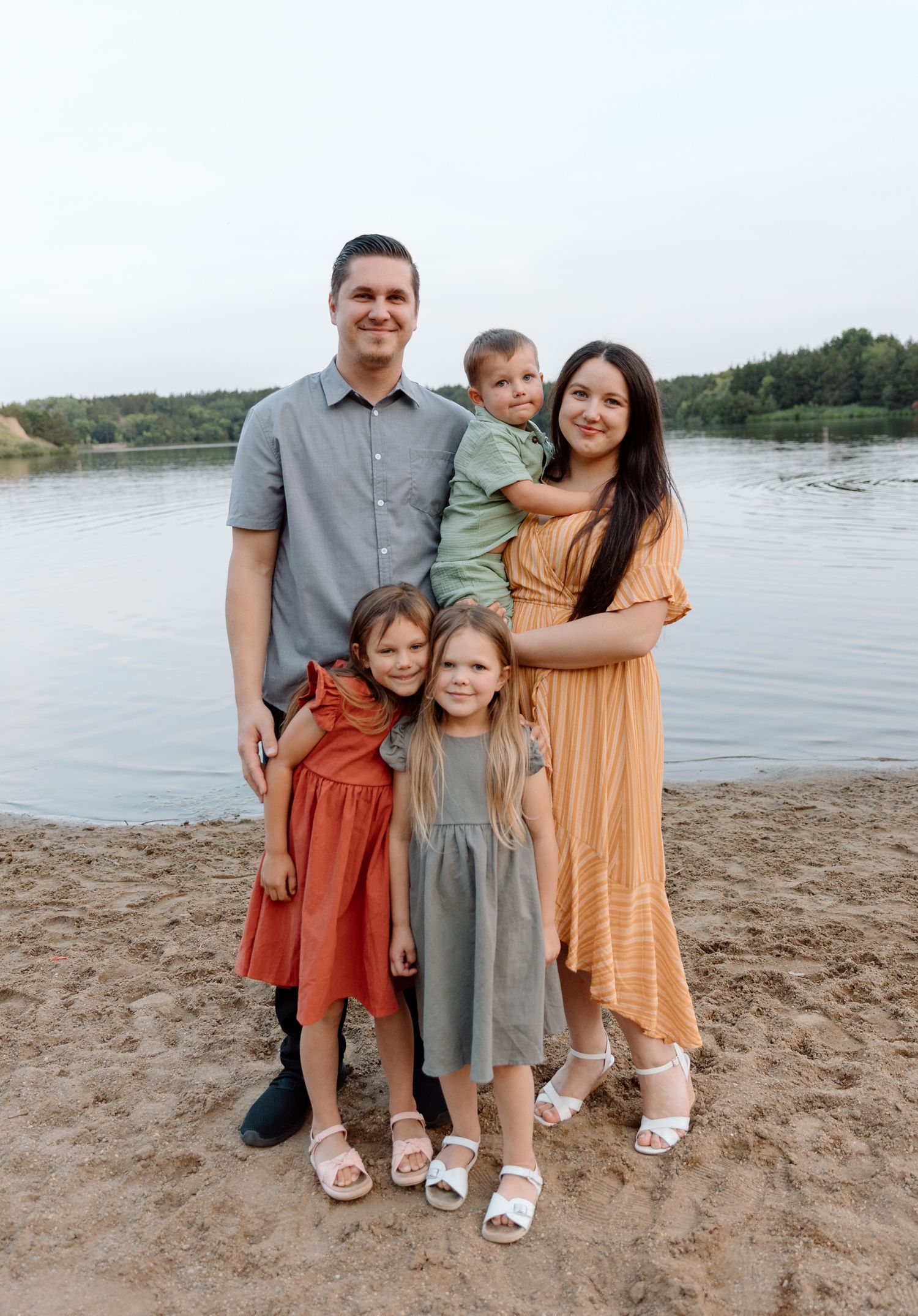 Family portrait at beach during sunset with coordinated casual outfits.