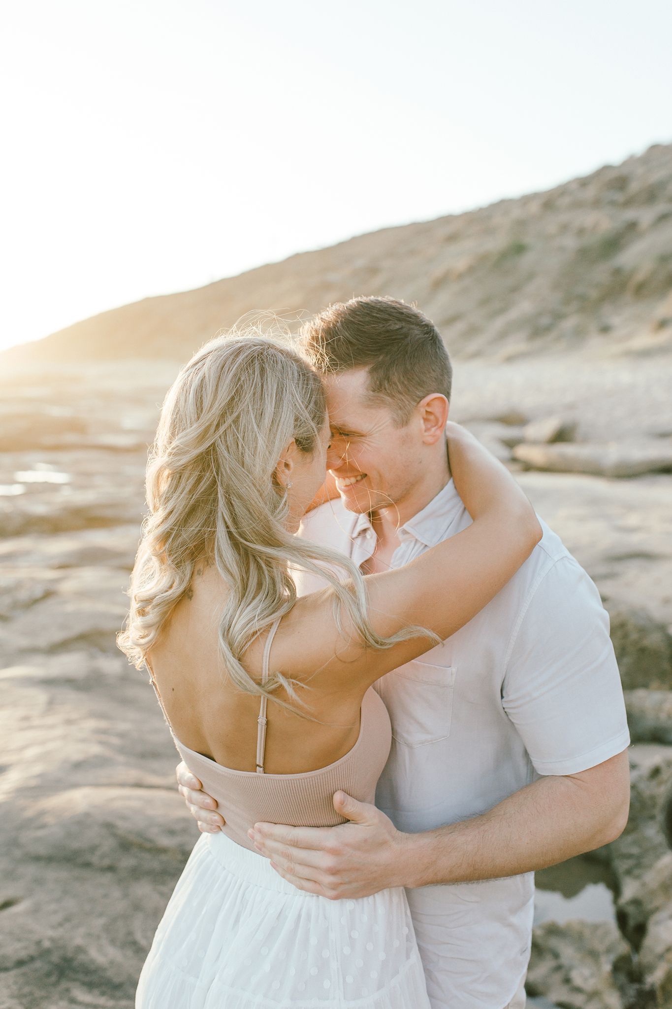 A couple shares an intimate moment on coastal rocks during sunset.