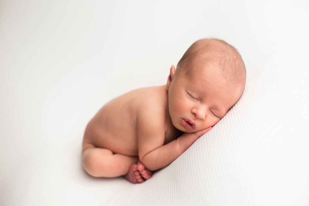 Newborn baby boy on white backdrop with toes under his elbows and hand under his cheek.