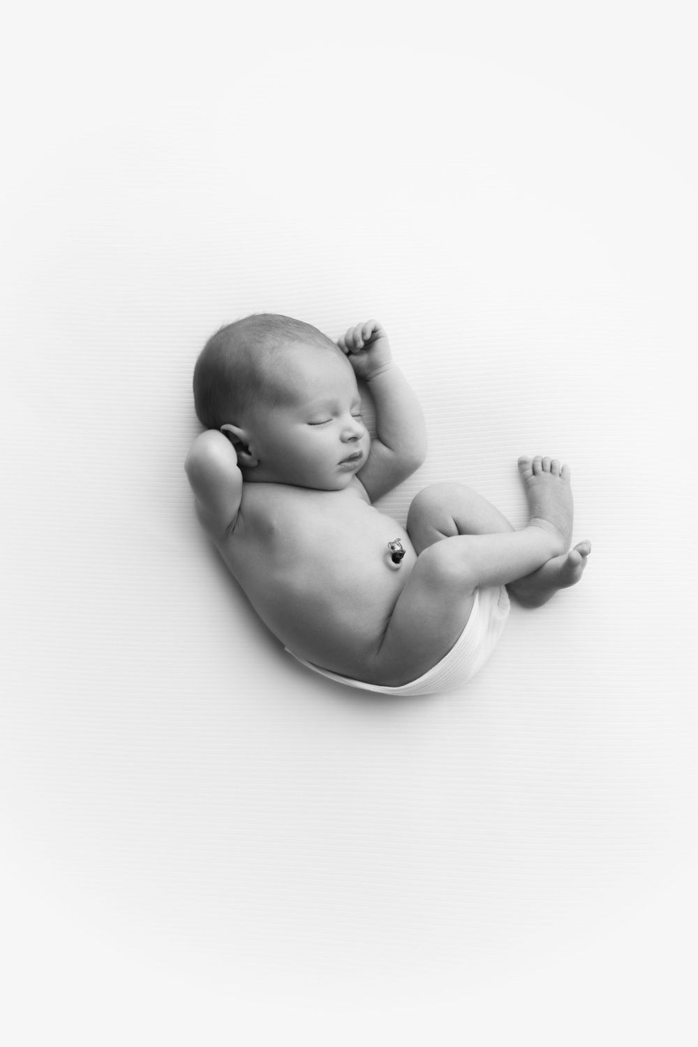 Newborn baby boy on white backdrop curled into a womb pose.