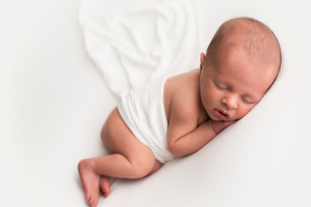 Newborn baby boy laying on his side with white wrap across his back.