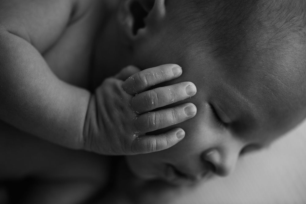 Black and white image of newborn baby boy with his hand on his chubby cheek.