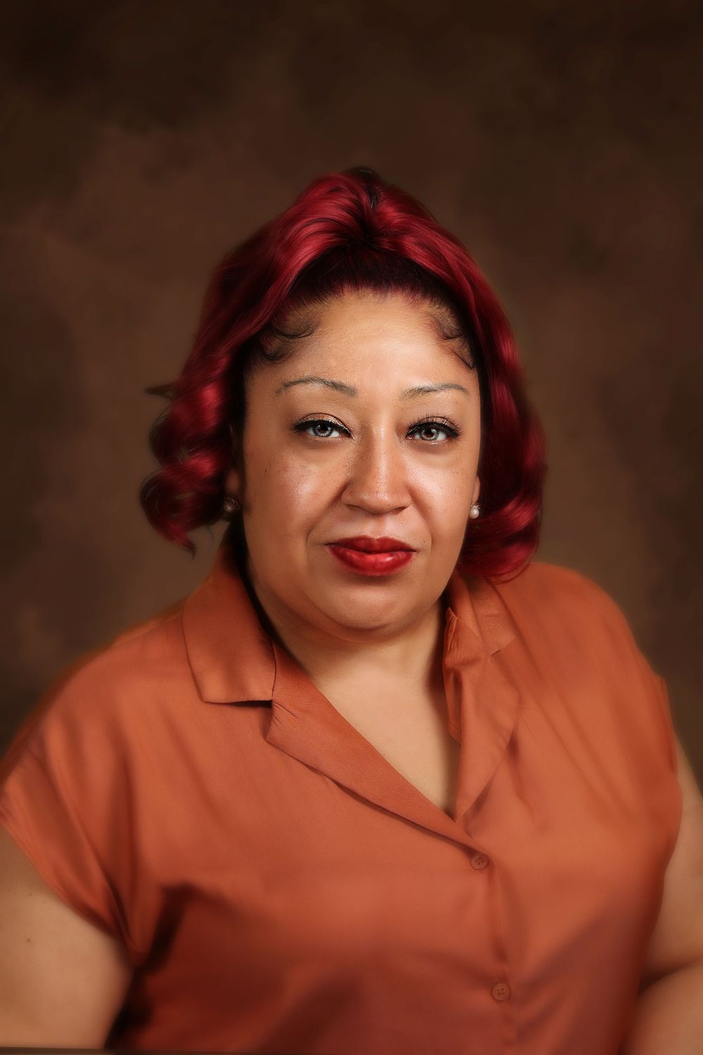 Studio portrait with vibrant red hair wearing coral colored blouse against brown background.